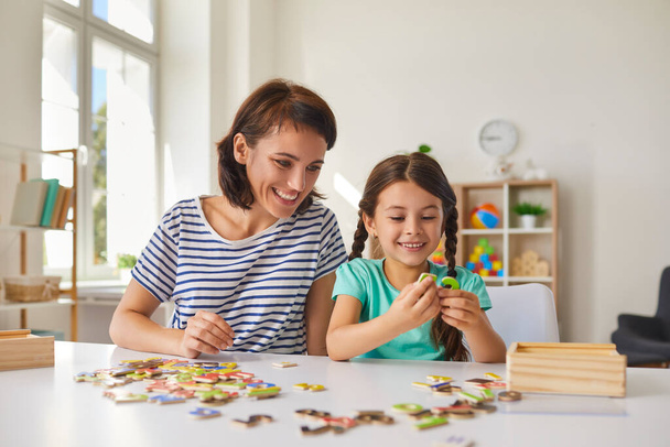 Mom and little daughter put together puzzles while sitting at a table in the room. - Foto, Bild