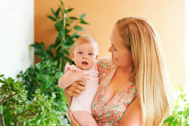 Jovem mãe feliz brincando com bebê adorável menina, família em casa, varanda verde aconchegante com muitas plantas em vasos - Foto, Imagem