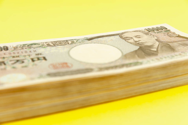 Deset tisíc jenů (deset tisíc jenů) na hromadě. Japonské peníze. Papírové peníze. Izolováno na žlutém pozadí. Boční pohled. Detailní záběr. - Fotografie, Obrázek