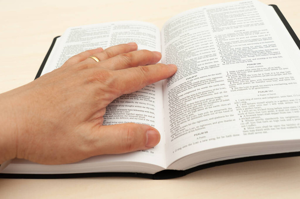 Ręka na Pismo Święte w zbliżeniu. Studiowanie i czytanie Słowa Bożego. Widok z góry. - Zdjęcie, obraz