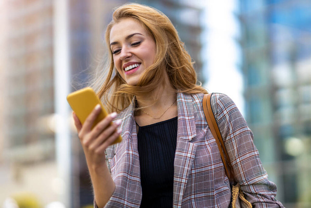 Ευτυχισμένη νεαρή γυναίκα που χρησιμοποιεί smartphone στην πόλη - Φωτογραφία, εικόνα