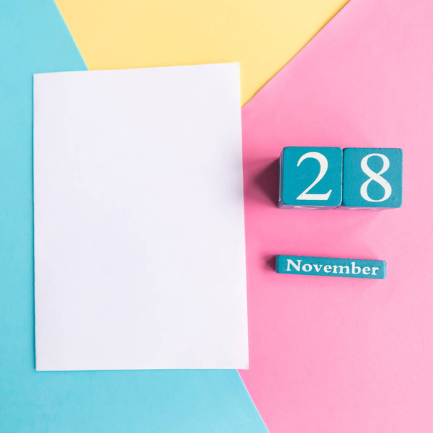 28 de noviembre. Calendario cubo azul con mes y fecha sobre fondo geométrico de color. - Foto, imagen