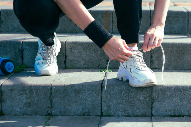 Girl ties her shoelaces on the stairs, close up. Outdoor sport activity - Photo, Image