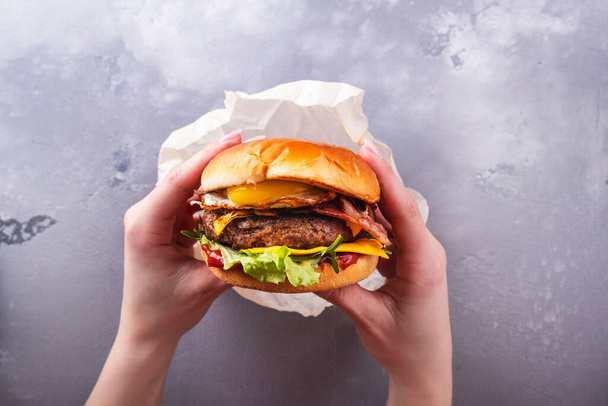 Ženské ruce držící chutný hovězí burger se smaženým vejcem. Horní pohled. Fastfood. Životní styl - Fotografie, Obrázek