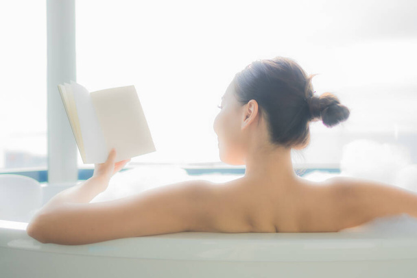 retrato bonito jovem asiático mulher ler livro no branco banheira no casa de banho interior - Foto, Imagem