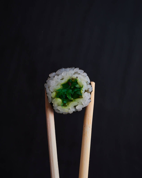 μπαμπού μπαστούνια κατέχουν σούσι ρολά σε σκούρο φόντο - Φωτογραφία, εικόνα