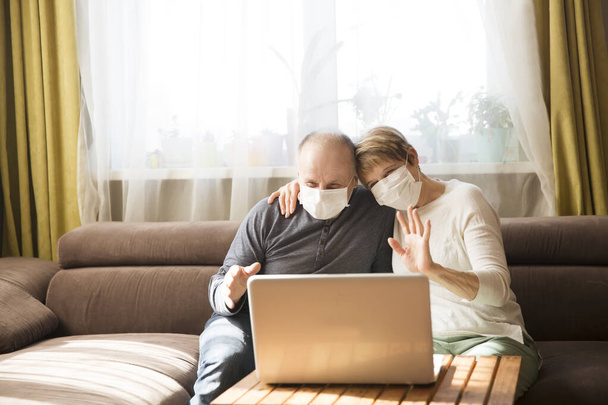 Seniors couple grandmother and grandfather wearing medical face masks  and using laptop Communicate with grandchildren online at home. quarantine. standing in home. chelter in place. - Foto, afbeelding