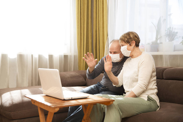 Seniors couple grandmother and grandfather wearing medical face masks  and using laptop Communicate with grandchildren online at home. quarantine. standing in home. chelter in place. - Foto, afbeelding