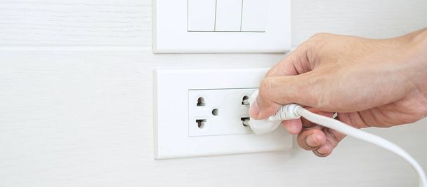 Крупним планом Чоловічий палець від'єднує або підключає електричний пристрій на білій стіні вдома. Енергозбереження, енергетика, електрика та концепції способу життя
 - Фото, зображення