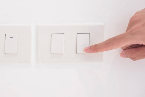 Primer plano El dedo masculino está encendido o apagado en el interruptor de luz en la pared blanca en casa. Conceptos de ahorro de energía, energía, electricidad y estilo de vida - Foto, imagen