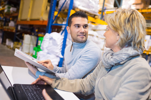 manager showing a clipboard to a worker in a warehouse - Foto, imagen