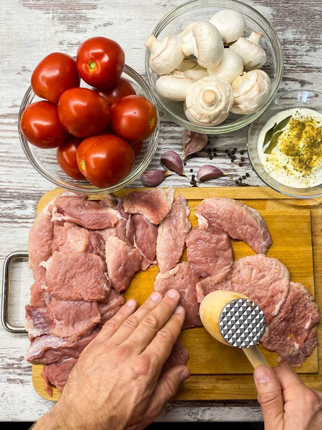Der Prozess des Zubereitens von Fleisch auf Französisch zu Hause. Großaufnahme männlicher Hände, die Schweinefleisch verprügeln. Konzept hausgemachter Lebensmittel, richtige Ernährung. - Foto, Bild