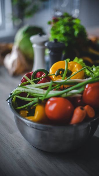 Close up Shot of a Gray Bowl Full of Fresh Healthy Vegetables Standing on a Kitchen Table. Natural Clean Products Prepared for Salad: Yellow Sweet Paper, Red Tomatoes, Green Onion, Carrot. - 写真・画像