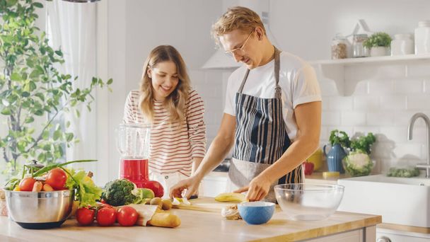 Handsome Young Man in Glasses Wearing Apron and Beautiful Girl are Making A Smoothie in the Kitchen. Happy Couple are Preparing Healthy Organic Beverage. Male and Female at Home on a Sunny Day. - Фото, зображення
