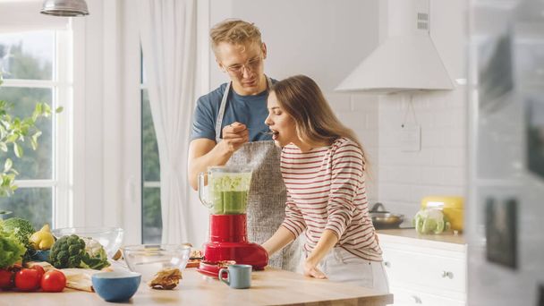 Handsome Young Man in Glasses Wearing Apron and Beautiful Girl are Making A Smoothie in the Kitchen. Happy Couple are Trying Healthy Organic Beverage. Male and Female at Home on a Sunny Day. - Foto, imagen