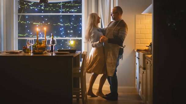 Senior Couple in Love Have Romantic Evening, Dancing in the Dining Room, Celebrating Anniversary. Portrait of a Happy Elderly Husband and Wife Have Lovely Evening with Festive Table in Cozy Kitchen - Foto, Imagem