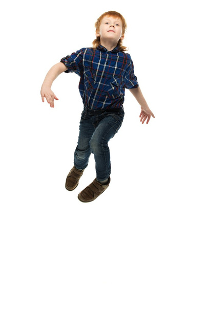 Little funny redhead boy in shirt and jeans jumping  - Zdjęcie, obraz