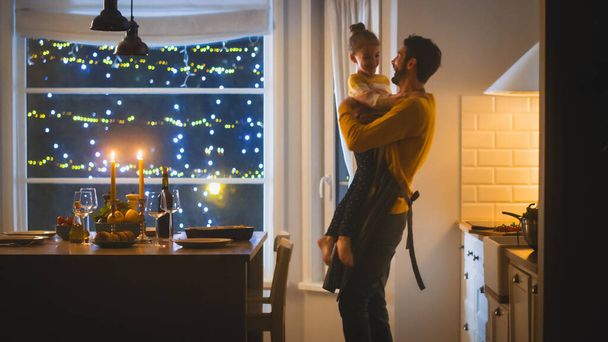 Happy Father and Daughter Cooking and Having Dinner Together. Father Prepares Food, Hugs Cute Little Girl. Festive Table in Stylish Kitchen Interior with Warm Light - Foto, Imagen