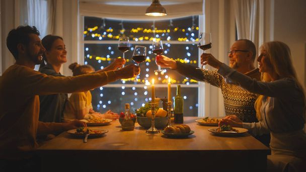 Happy Family Celebrating together, Sitting at the Table Eating Delicious Dinner Meal. Little Child, Young Husband, Wife, Grandfather and Grandmother, Telling Stories, Joking, Raising Glasses to Toast - 写真・画像
