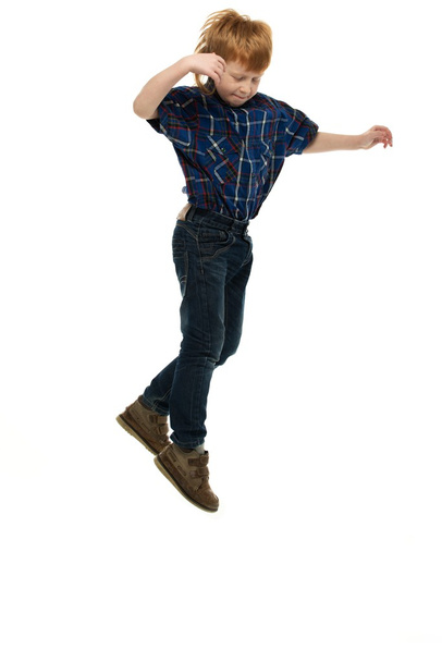 Little funny redhead boy in shirt and jeans jumping  - 写真・画像