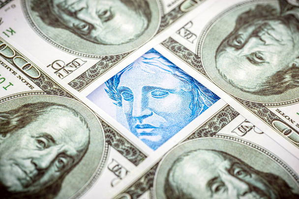 detalle de un billete de cien reales de Brasil, atrapado entre billetes de 100 dólares americanos. Crisis económica y alza de la moneda estadounidense - Foto, Imagen