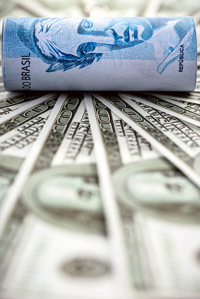 dinero americano que rodea un billete de cien reales de Brasil, concepto de bajo real en el mercado mundial - Foto, Imagen