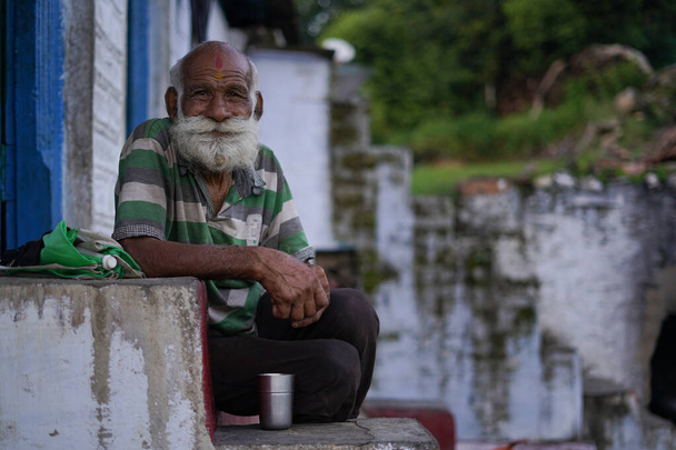 Ein alter indischer Mann mit langem und weißem Bart sitzt auf der Treppe und trägt robuste Kleidung. - Foto, Bild
