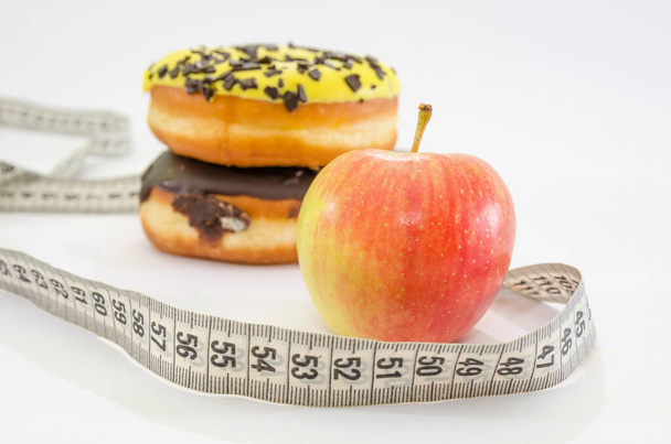 choice between apple or junk food, donut. Diet and healthy food concept. Vegetarian, vegan,. Apple, measuring tape and donuts and on white - Photo, image