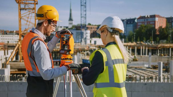 Construction Worker Using Theodolite Surveying Optical Instrument for Measuring Angles in Horizontal and Vertical Planes on Construction Site. Engineer and Architect Using Tablet Next to Surveyor. - Фото, изображение