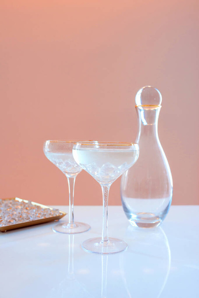  glass decanter, elegant glasses with cocktail and ice on beige background. Alcohol, water, party, hotel, bar concept - Foto, Bild