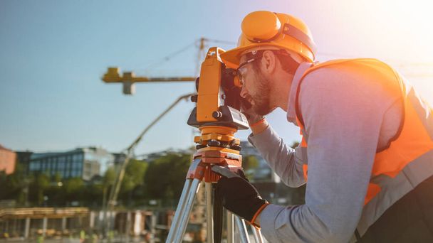 Construction Worker Using Theodolite Surveying Optical Instrument for Measuring Angles in Horizontal and Vertical Planes on Construction Site. Worker in Hard Hat Making Projections for the Building. - Zdjęcie, obraz