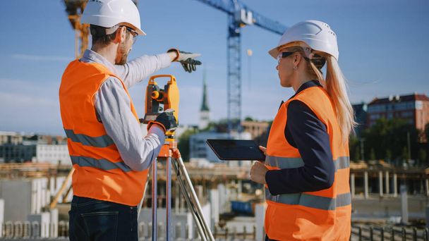 Construction Worker Using Theodolite Surveying Optical Instrument for Measuring Angles in Horizontal and Vertical Planes on Construction Site. Engineer and Architect Using Tablet Next to Surveyor. - Foto, afbeelding