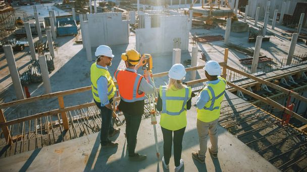 Construction Worker Using Theodolite Surveying Optical Instrument for Measuring Angles in Horizontal and Vertical Planes on Construction Site. Engineers and Architect Discuss Plans Next to Surveyor. - Foto, afbeelding