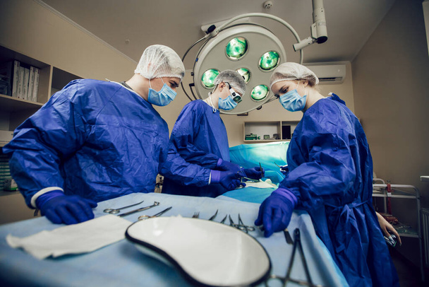 Retrato del equipo de cirujanos en el trabajo. Tres médicos con máscaras médicas en operaciones comienzan a operar al paciente. Médicos en cirugía, tratamiento y medicina - Foto, imagen