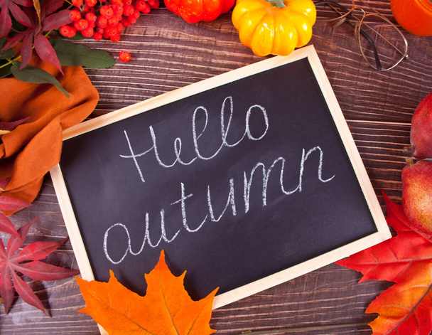 Chalkboars with Hello autumn text. Composition with pumpkin, autumn leaves, cadle and red pears on the wooden background. Cozy autumn mood concept - Foto, Bild