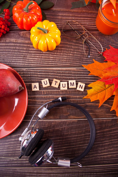 Greeting card with Autumn text. Composition with pumpkin, autumn leaves, headphones, candle and red pears on the wooden background. Cozy autumn mood concept - Photo, Image