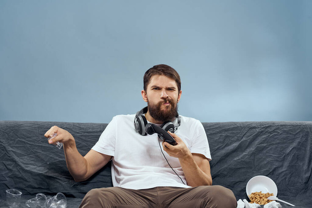 Uomo seduto sul divano indossando cuffie con gamepad giocare cibo tempo libero tecnologia stile di vita - Foto, immagini