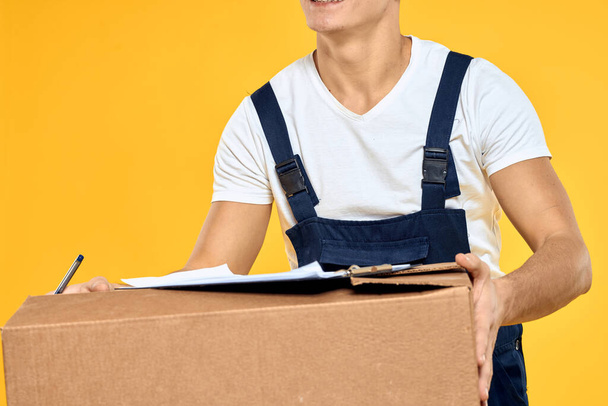 Munkás ember egyenruhában doboz kézzel szállítási rakodási szolgáltatás sárga háttér - Fotó, kép