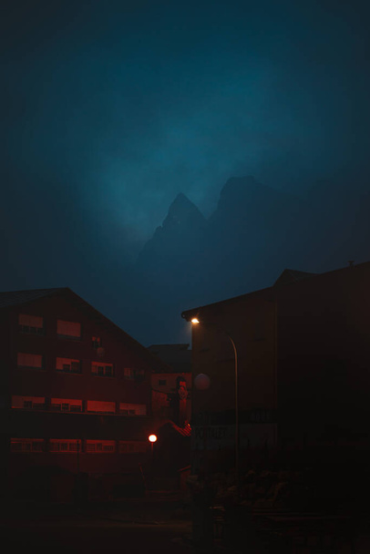 Σιλουέτα ενός μεγάλου βουνού πίσω από δύο κτίρια σε μια ανατριχιαστική πόλη - Φωτογραφία, εικόνα