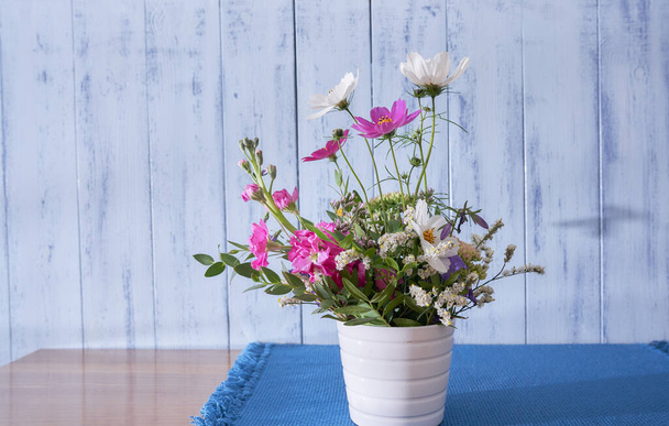   colorful wildflowers stand on a wooden table in a white vase against a blue wall                                       - Foto, afbeelding