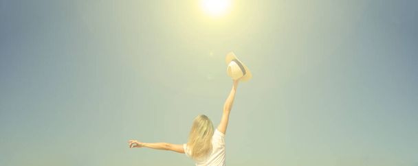 Vista trasera de una mujer sosteniendo un sombrero contra un cielo azul - Foto, Imagen