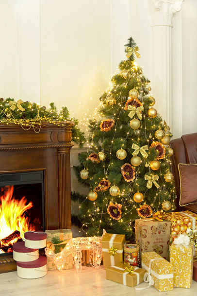Christmas and New Year. Colorful Christmas fir-tree, golden christmas decorations and gifts near fireplace in home interior. - Foto, imagen