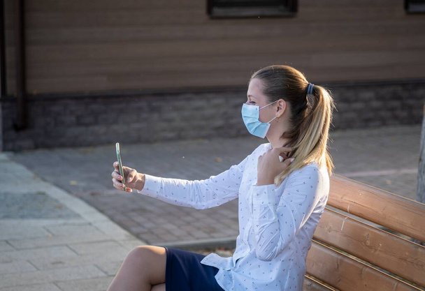 Egy fiatal hölgy orvosi maszkban csinál egy szelfit az okostelefonjával. a karantén koncepciója, maszkos üzemmód a kovid-19 járvány idején - Fotó, kép
