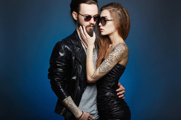 lovely beautiful couple in sunglasses.bearded Hipster boy and beauty girl with tattoo over blue background - Photo, Image
