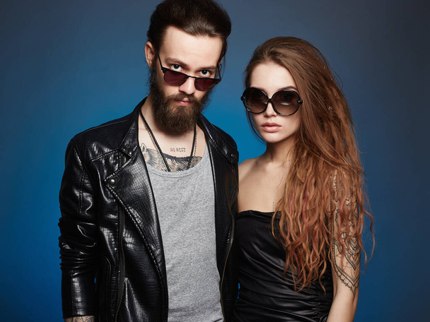 красива пара в сонцезахисних окулярах. бородатий хлопчик-хіпстер і дівчина краси з татуюванням на синьому фоні
 - Фото, зображення