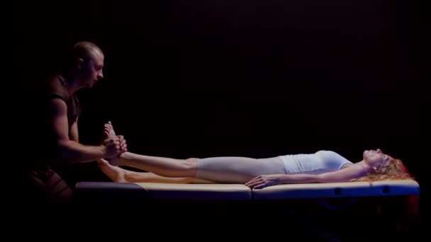 Sesja z kręgarzem - młoda kobieta leżąca na plecach i terapeutka nagle wyciąga nogę w swoją stronę - Materiał filmowy, wideo