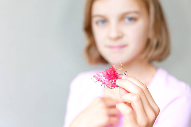 Dívka drží v rukou růžový ortodontický talíř a ukazuje ho. - Fotografie, Obrázek