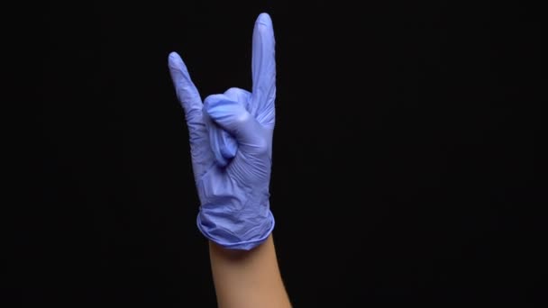 La mano femenina en un guante médico de látex hace un gesto rocoso aislado sobre fondo negro - Imágenes, Vídeo
