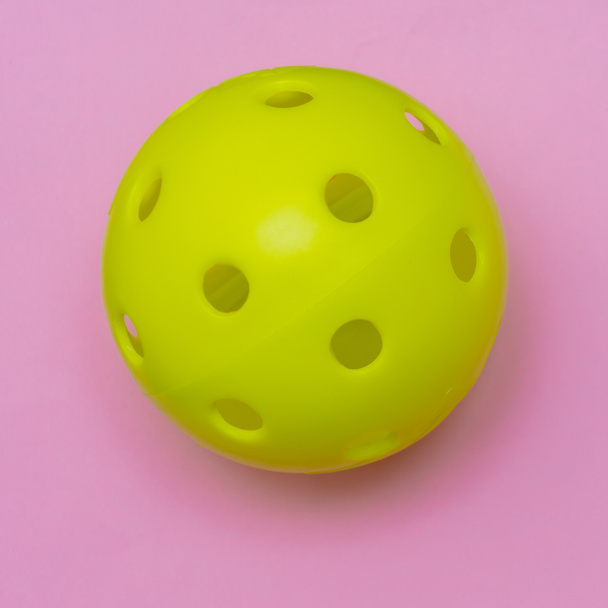 Escabeche amarillo brillante o bola del whiffle en un fondo plano rosado brillante sólido de la disposición que simboliza deportes y actividad con espacio de la copia. - Foto, imagen
