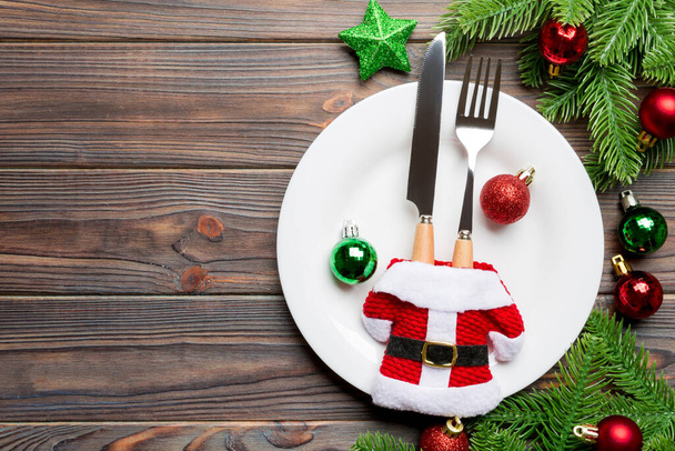 Çatal, bıçak ve tabağın üst görüntüsü köknar ağacı ve ahşap arka planda Noel süslemeleri ile çevrili. Yeni yıl arifesi ve tatil yemeği konsepti. - Fotoğraf, Görsel